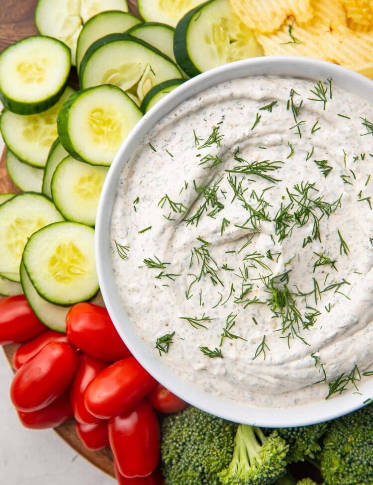 A bowl of dill dip surrounded by veggies