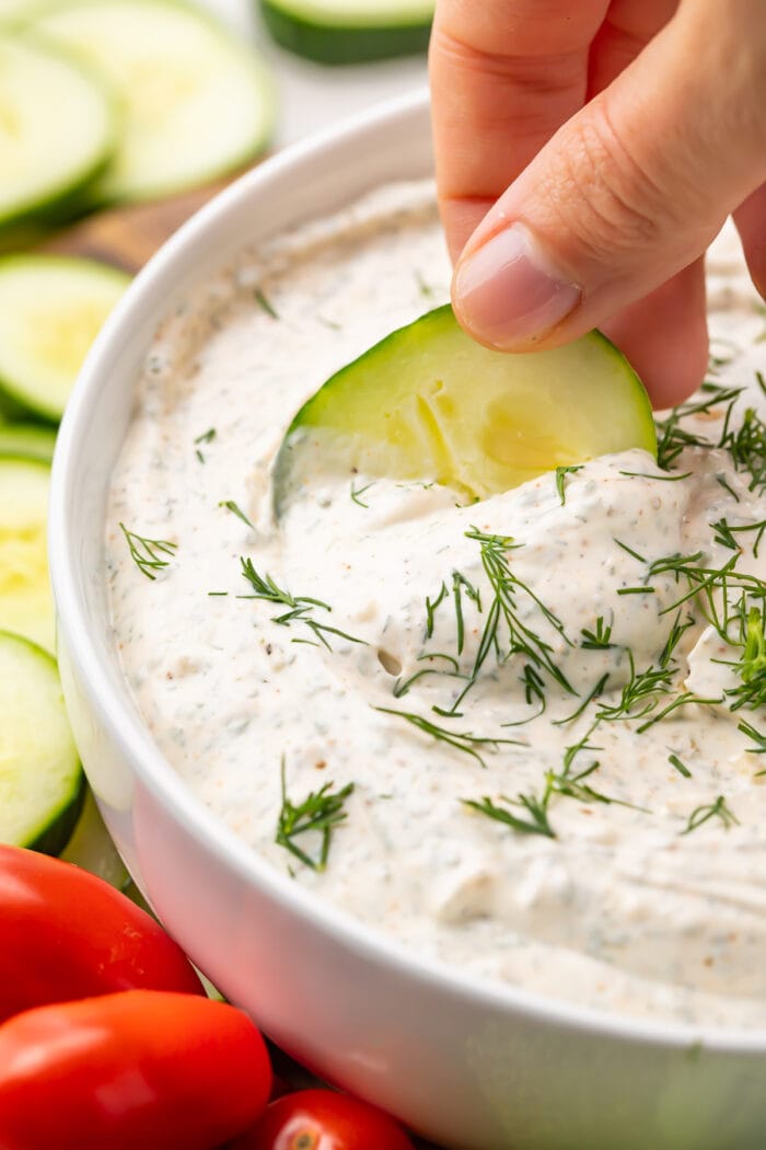 Cucumber dipped into a bowl of dill dip