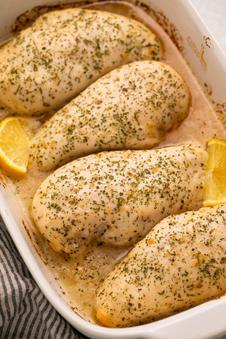 4 large chicken breasts baked with Italian dressing and garnished with lemon wedges in a large baking dish.