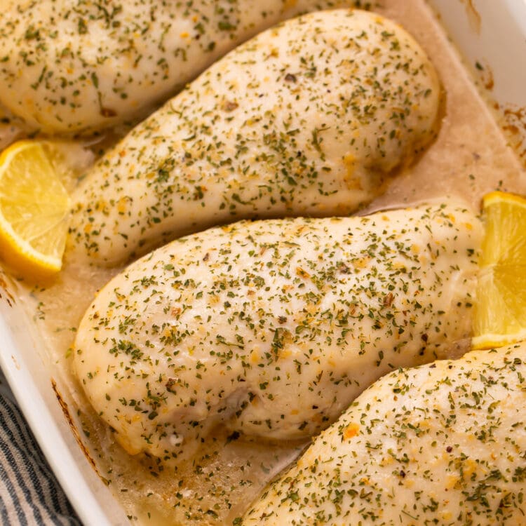 4 large chicken breasts baked with Italian dressing and garnished with lemon wedges in a large baking dish.