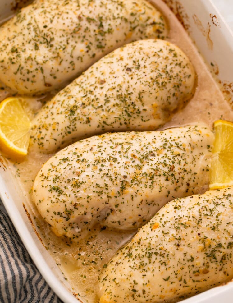 4 large chicken breasts baked with Italian dressing and garnished with lemon wedges in a large baking dish.