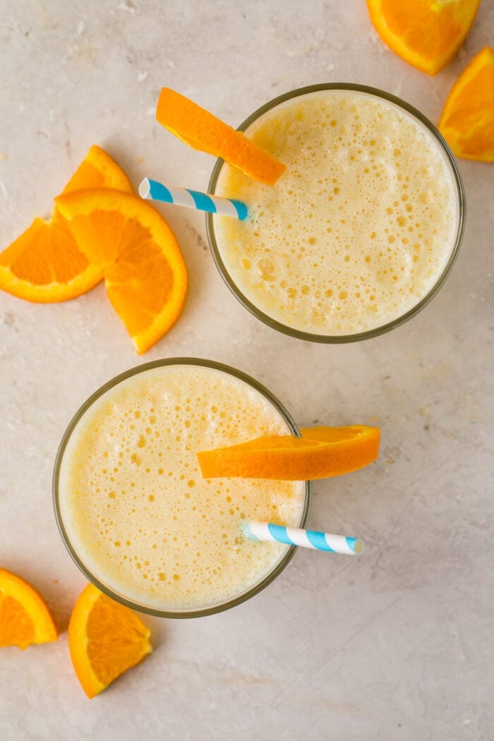 Overhead image of two glasses of Orange Julius with orange wedge garnishes and blue and white striped straws