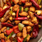 Top-down view of a large wok holding prepared Szechuan chicken with cashews, chilies, peppercorns, and chicken.
