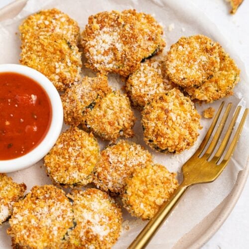 Air Fryer Zucchini Chips on a plate, sprinkled with parmesan cheese and served with marinara sauce.