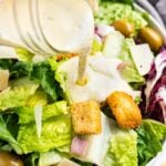 Creamy Italian dressing being poured over a salad with croutons and parmesan cheese.