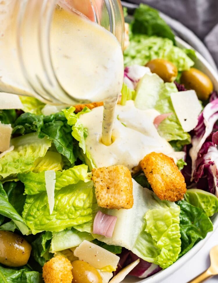 Creamy Italian dressing being poured over a salad with croutons and parmesan cheese.