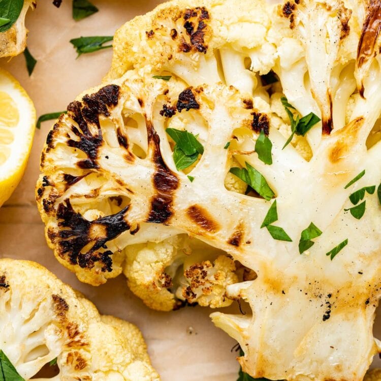 Close-up image of grilled cauliflower on parchment paper sprinkled with fresh parsley.