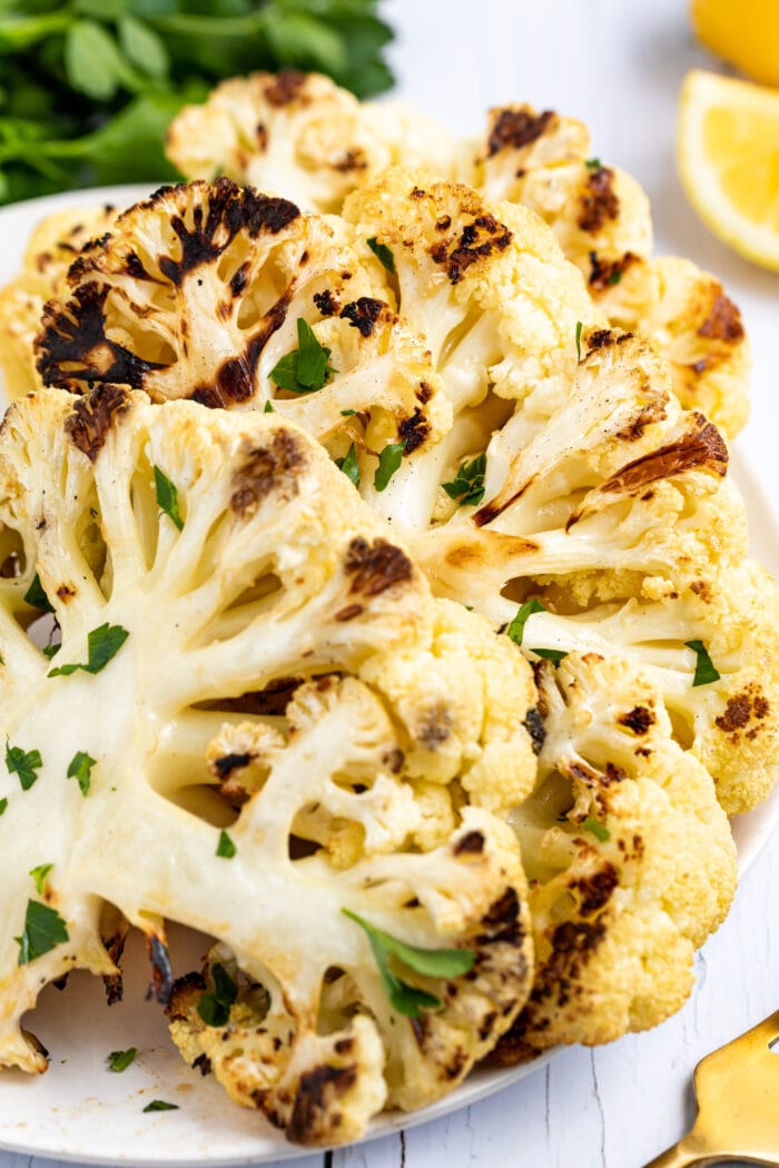 Grilled cauliflower assembled on a plate with lemon slices and fresh parsley on the side.