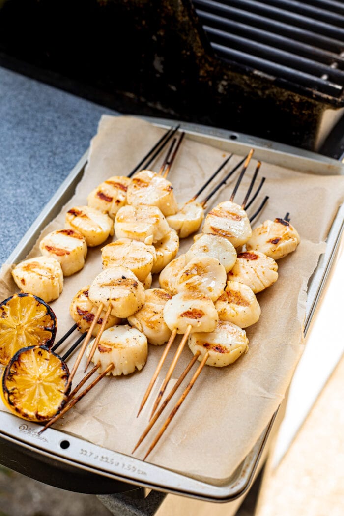Fully cooked grilled scallops sitting on a baking sheet next to a grill.