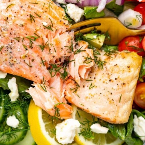 fork cutting into a salmon filet over salad.