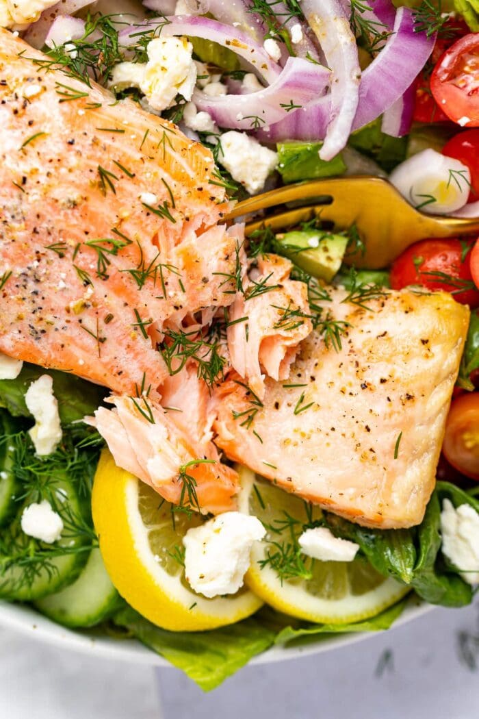 fork cutting into a salmon filet over salad.