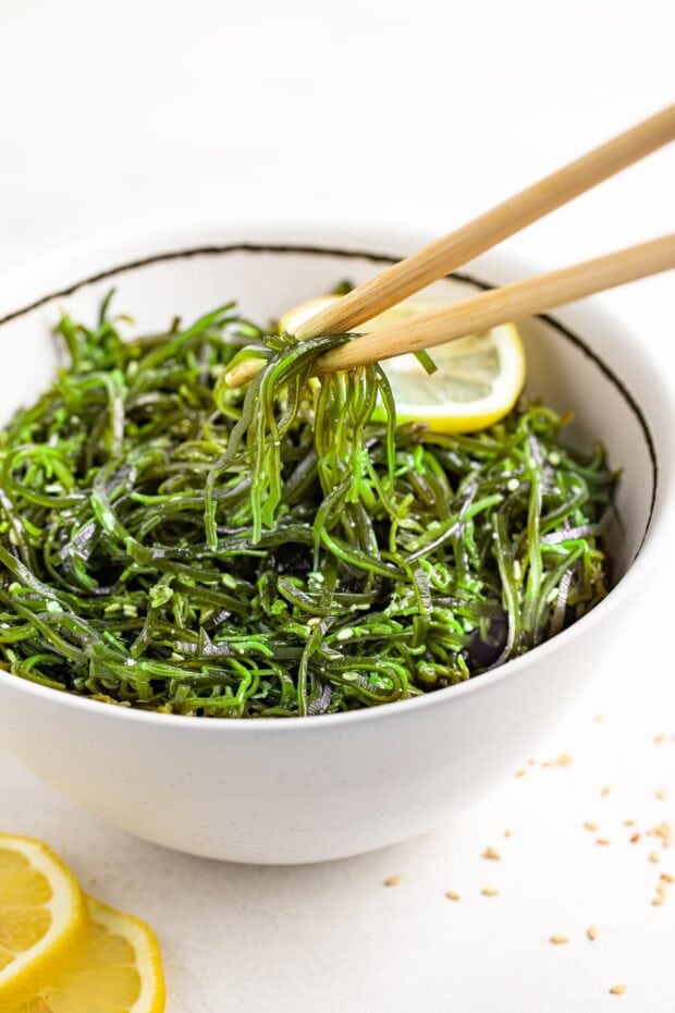 seaweed salad being lifted out of a bowl with chopsticks