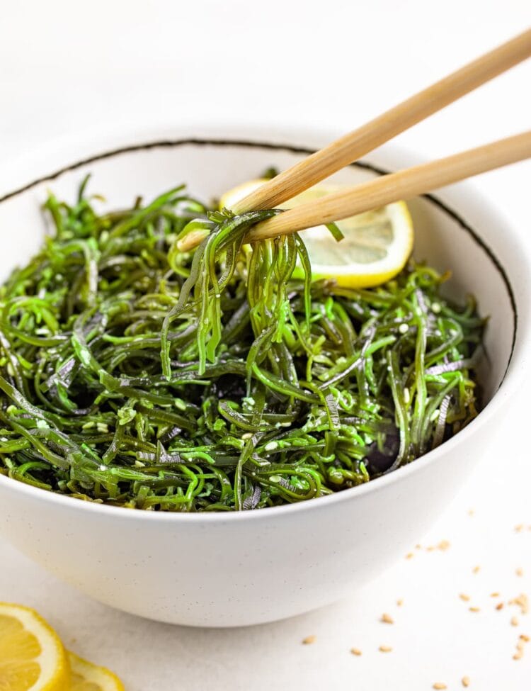 seaweed salad being lifted out of a bowl with chopsticks