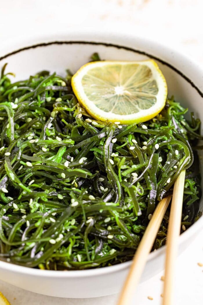 seaweed salad in a bowl with chopsticks, topped with sesame seeds and a lemon slice.
