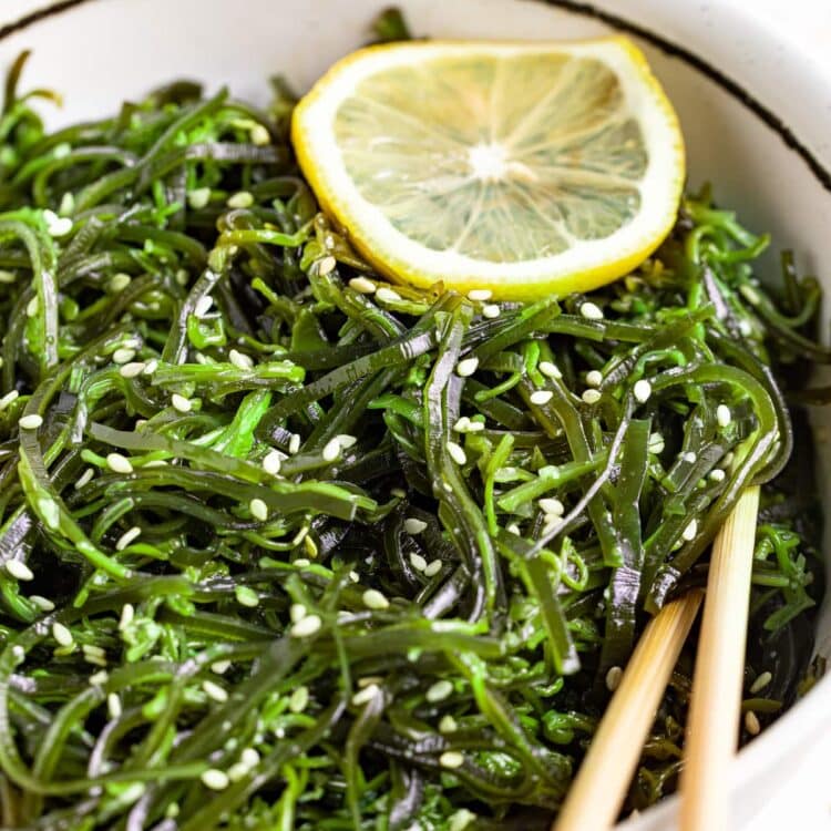 seaweed salad in a bowl with chopsticks, topped with sesame seeds and a lemon slice.