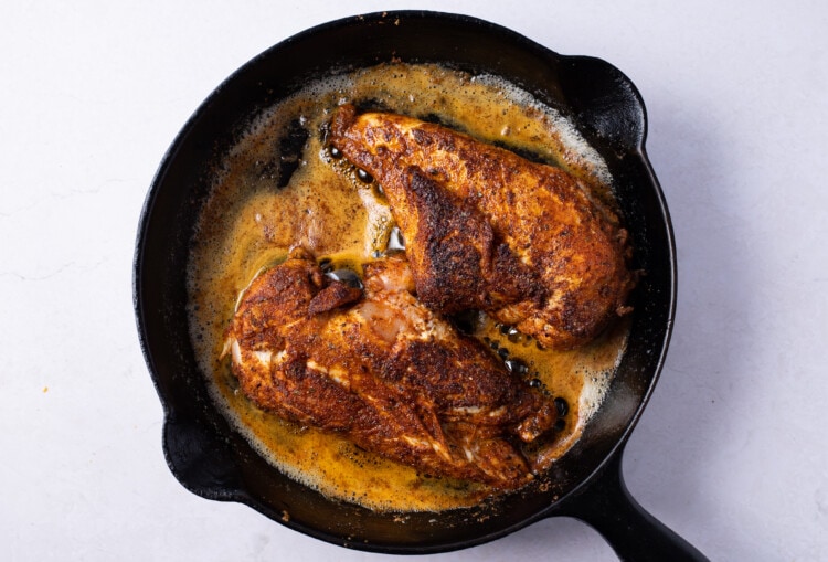 Blackened chicken breasts in cast iron skillet with melted butter