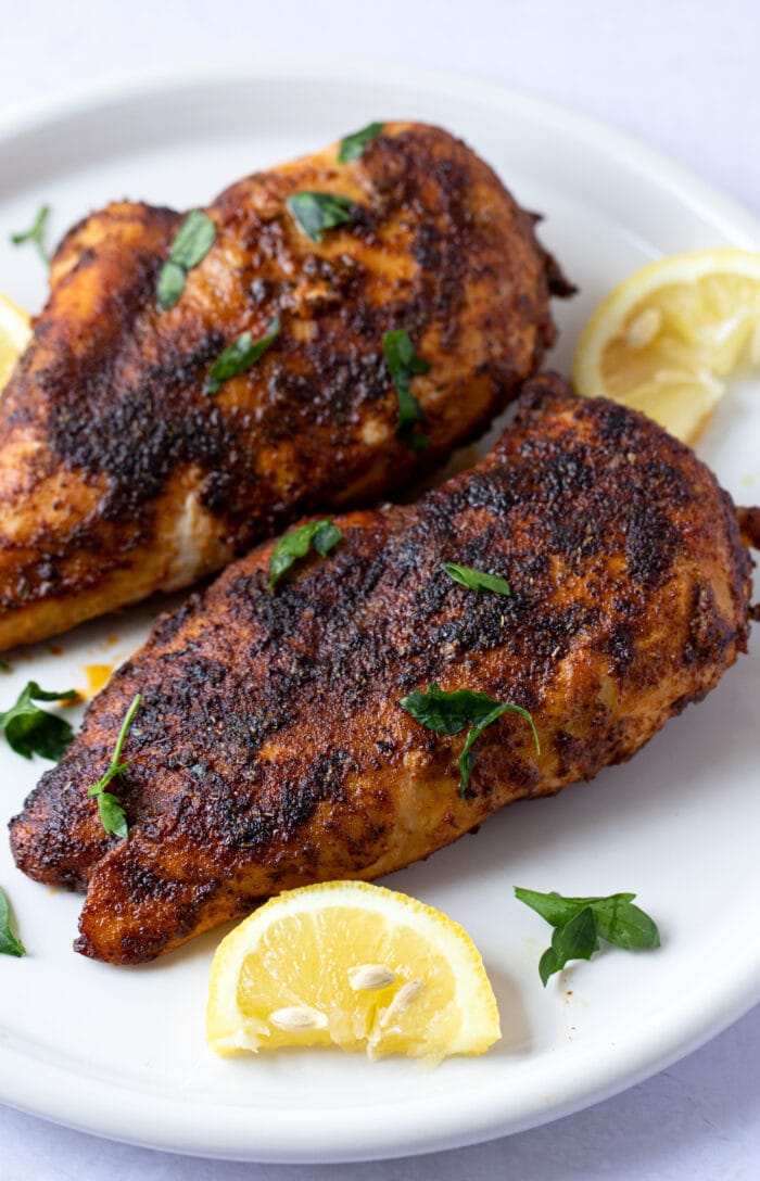 Blackened chicken on a white plate with lemon wedge garnish