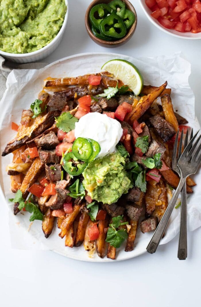 Overhead angle of carne asada fries on a plate with sour cream and guacamole
