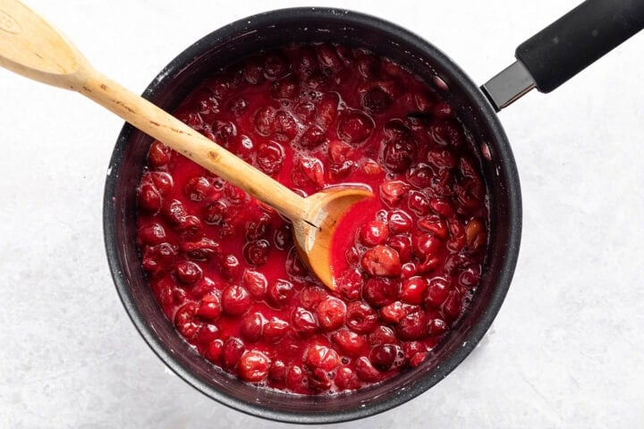 Cherry filling in a medium saucepan with a largen wooden spoon.