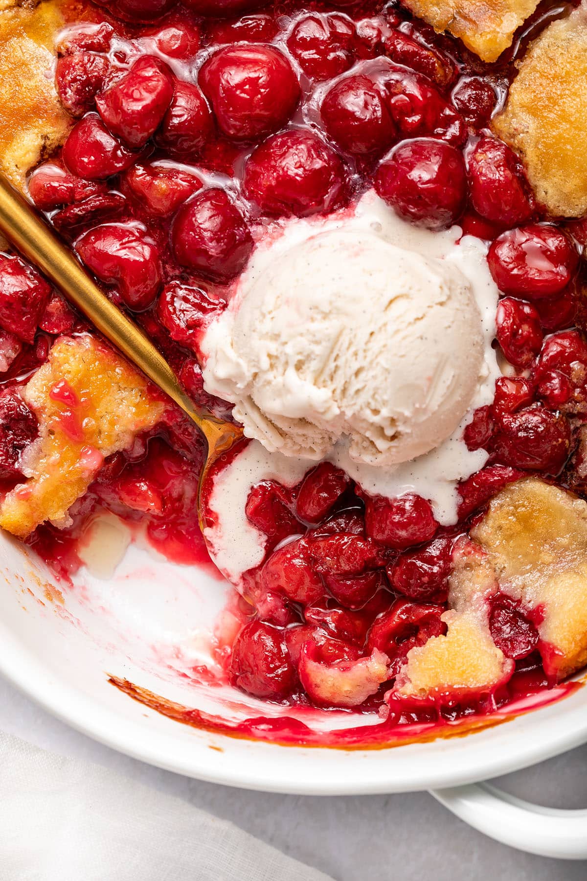 A baking dish of cherry cobbler topped with a scoop of vanilla ice cream.
