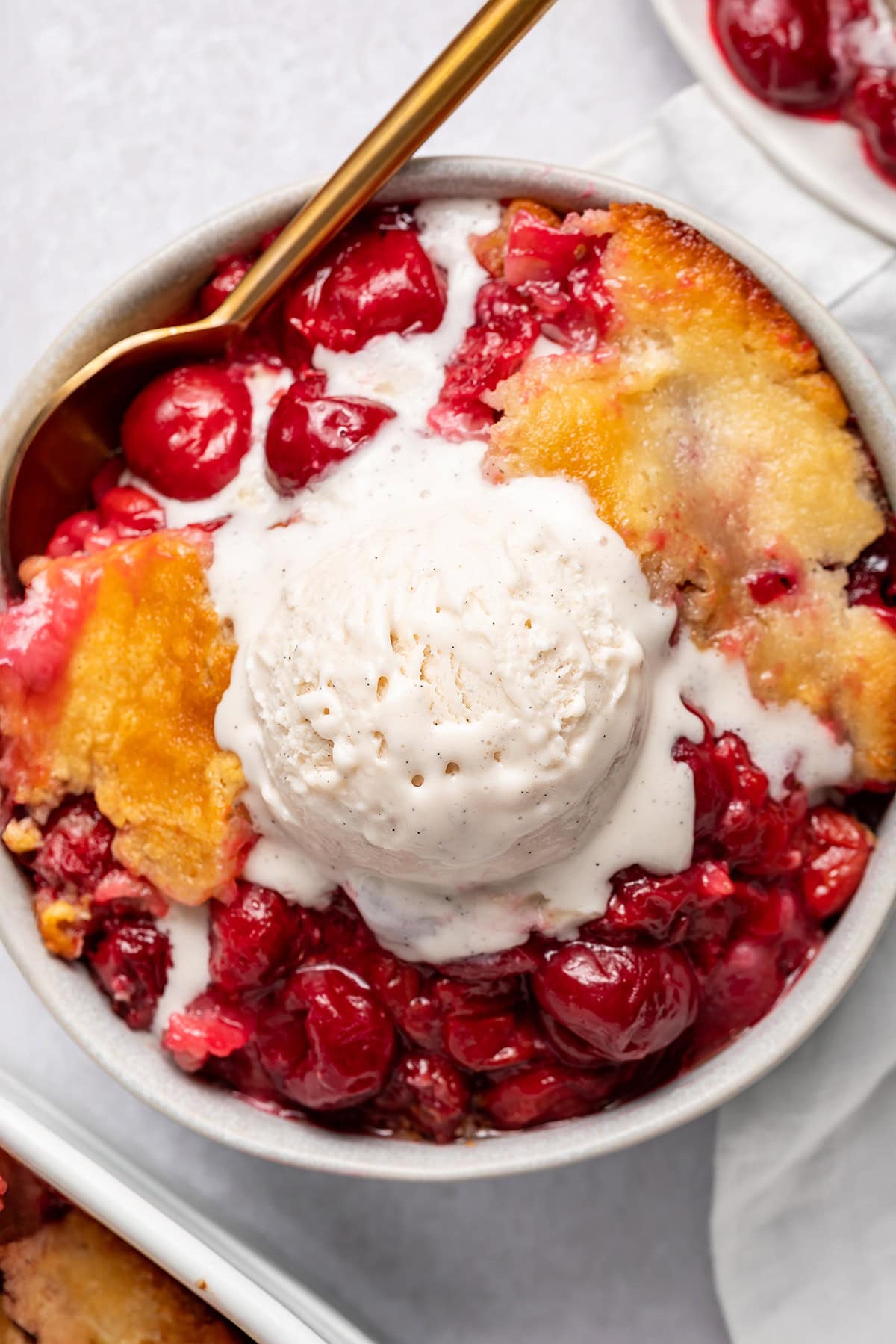 A large bowl of cherry cobbler topped with a scoop of vanilla ice cream that's melting slightly.