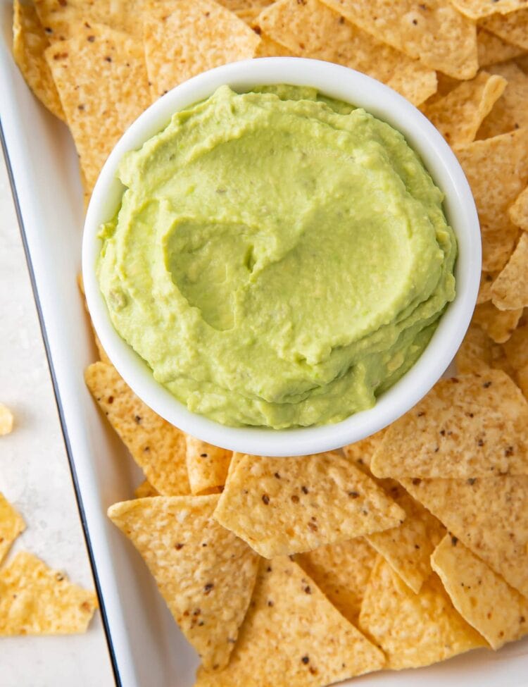 Guacamole dip in a bowl on a platter with tortilla chips