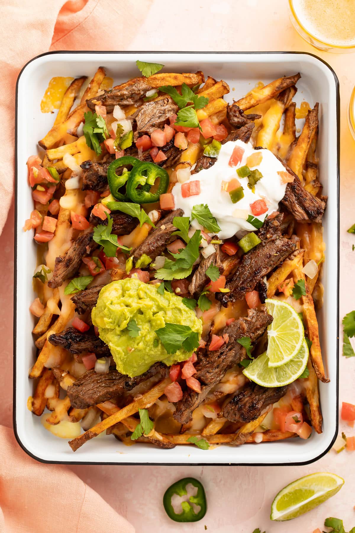 A sheet pan of loaded carne asada fries topped with guacamole, sour cream, cheese, and green onions.