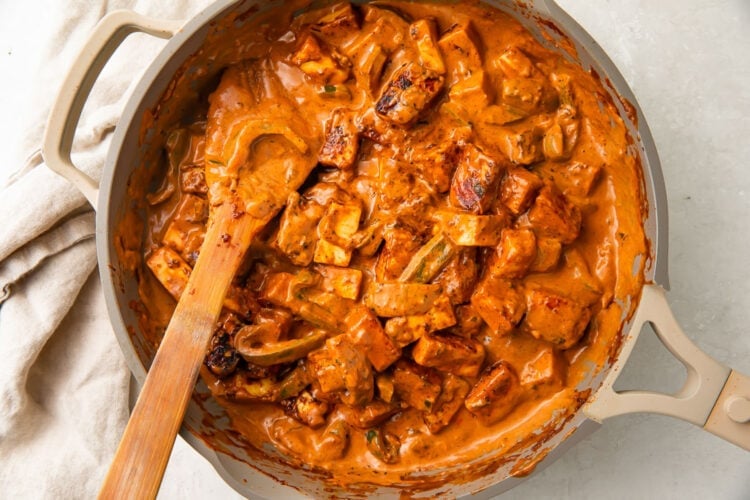Paneer tikka masala in a large skillet with a large wooden spoon.