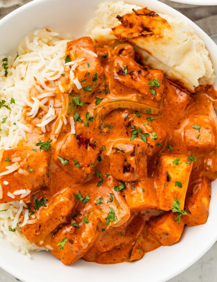 Deep orange paneer tikka masala in a white bowl with white rice and a piece of naan.