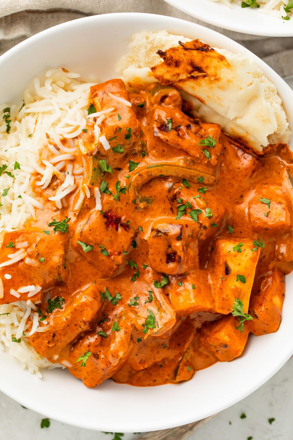 Deep orange paneer tikka masala in a white bowl with white rice and a piece of naan.