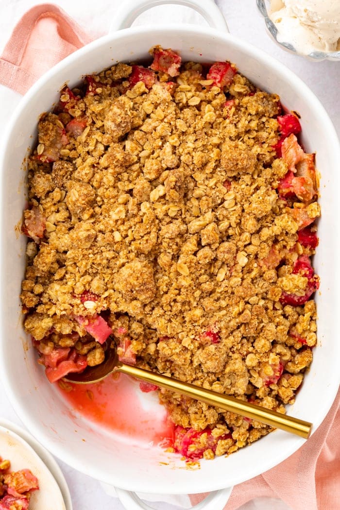 Overhead picture of rhubarb crumble in baking dish with a scoop removed and ice cream on the side.