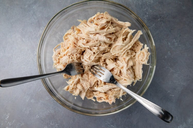 Shredded chicken in glass bowl with 2 forks