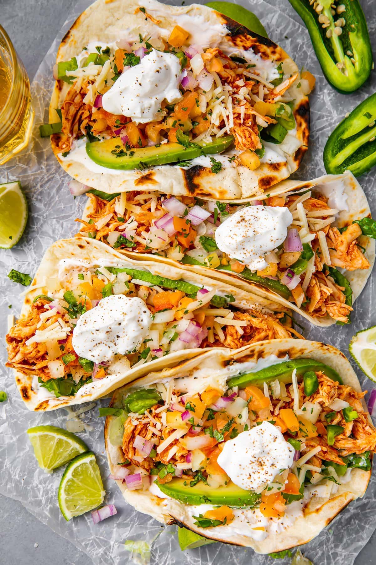 Four shredded chicken tacos arranged on a sheet of parchment paper.