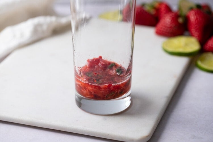 Muddled strawberries, mint leaves, and simple syrup in a highball glass