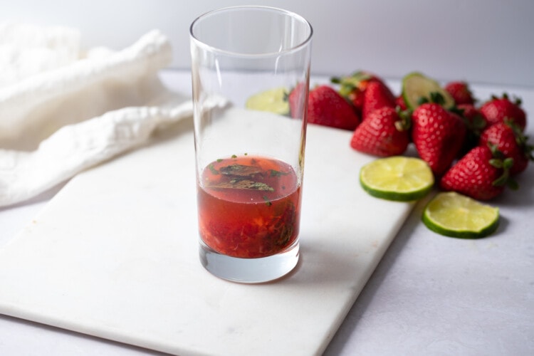 Lime juice and rum in a highball glass with muddled strawberries