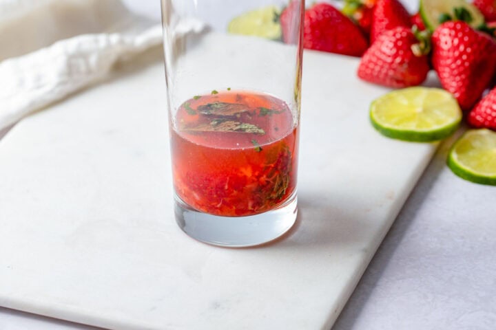 Lime juice and rum in a highball glass with muddled strawberries and mint leaves.