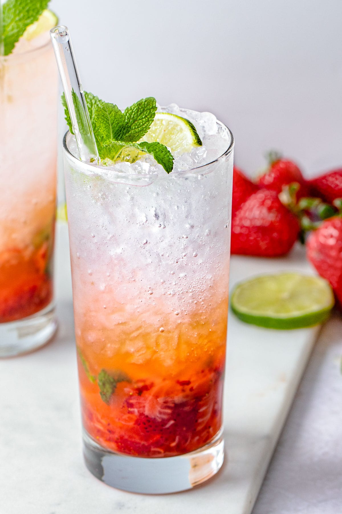 A tall highball glass containing a strawberry mojito, with rum and ice layer on top of muddled strawberries and mint.
