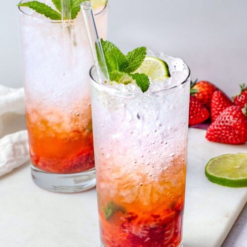 A tall highball glass containing a strawberry mojito, with rum and ice layer on top of muddled strawberries and mint.