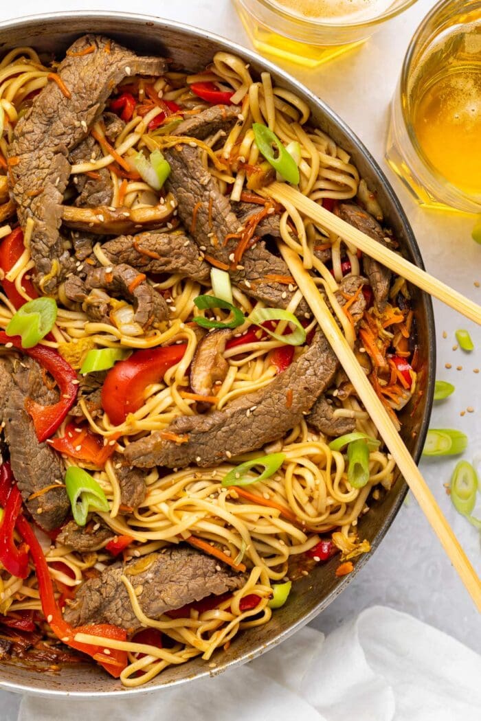 beef lo mein in a skillet with slice green onion and sesame seeds on top