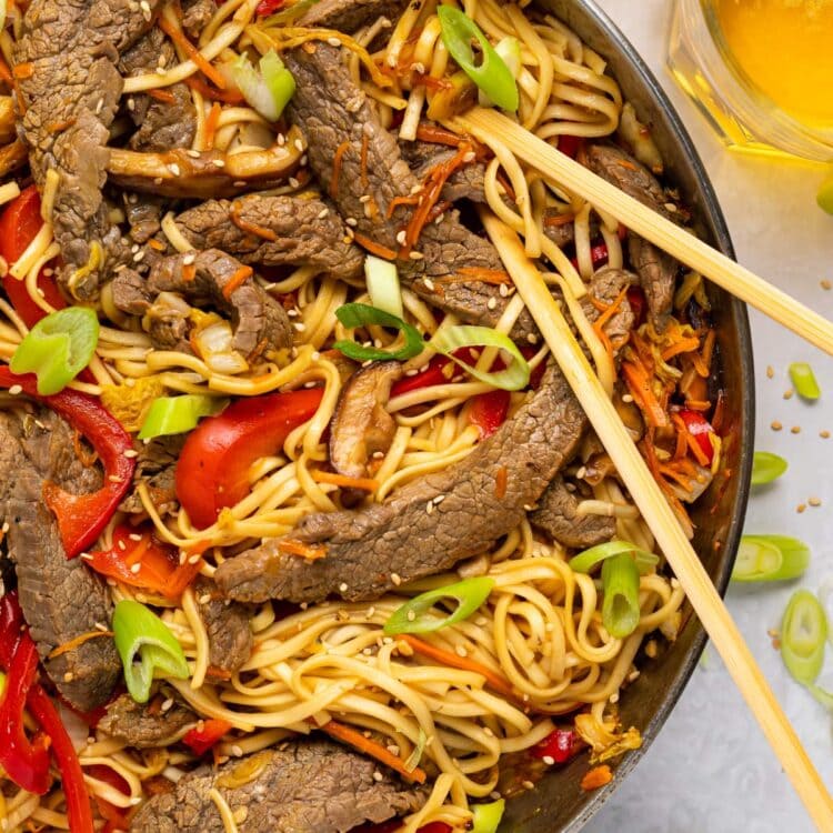 beef lo mein in a skillet with slice green onion and sesame seeds on top