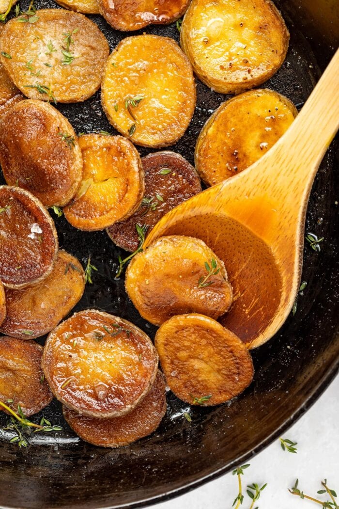 crispy pan fried potatoes being lifted out of a pan with a spoon