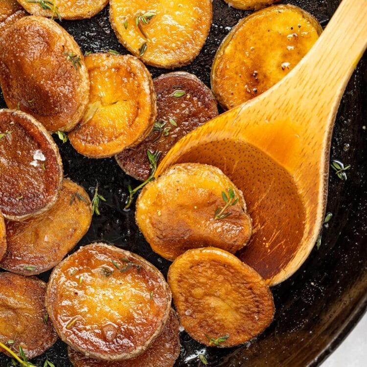 crispy pan fried potatoes being lifted out of a pan with a spoon