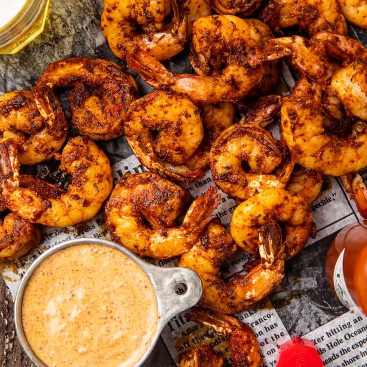 A pile of blackened shrimp on newspaper next to a dipping cup of remoulade sauce