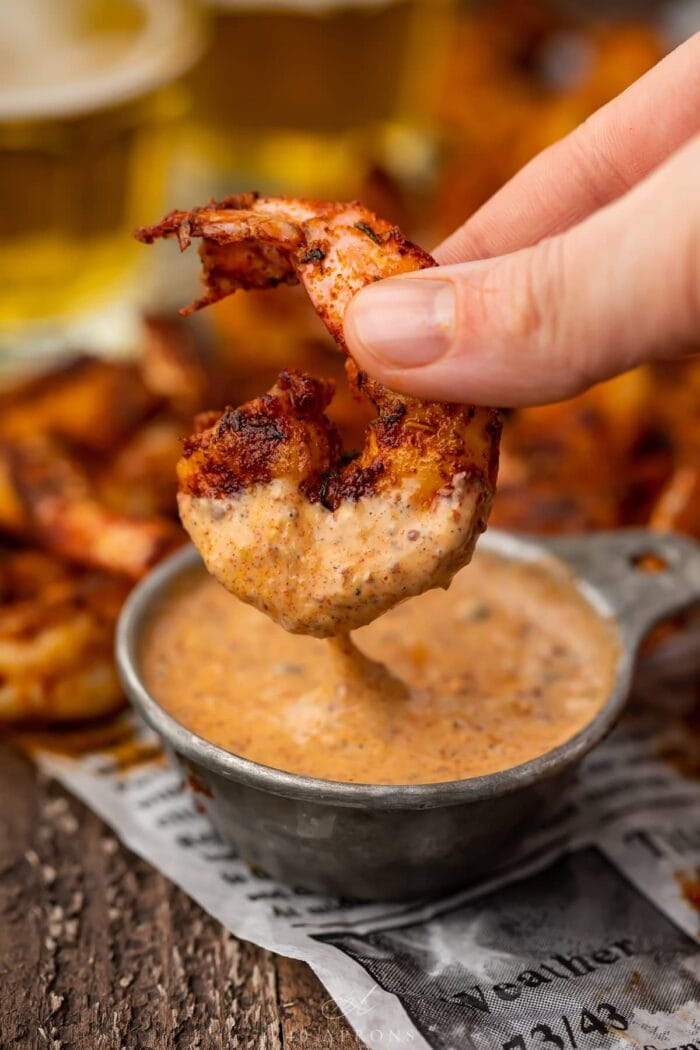 A single blackened shrimp being dipped into a small bowl of remoulade