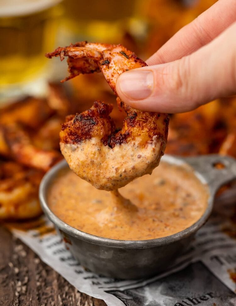 A single blackened shrimp being dipped into a small bowl of remoulade