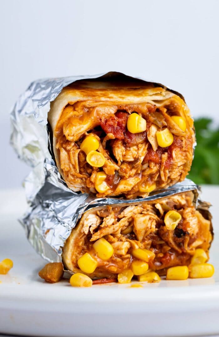 Two chicken burritos stacked on top of each other, cut crosswise to show chicken, corn, refried beans, and tomatoes inside