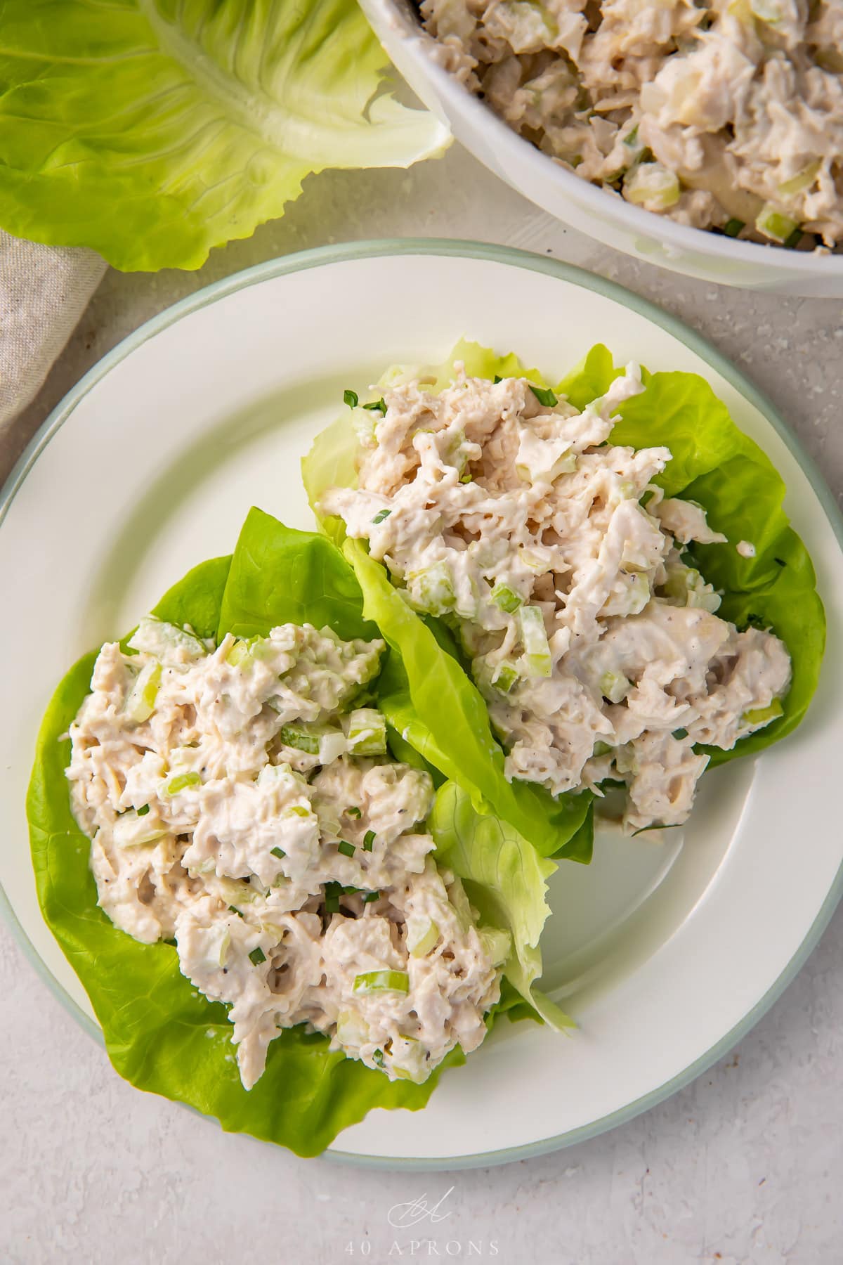 Keto chicken salad in lettuce wraps on a plate next to a bowl of chicken salad.
