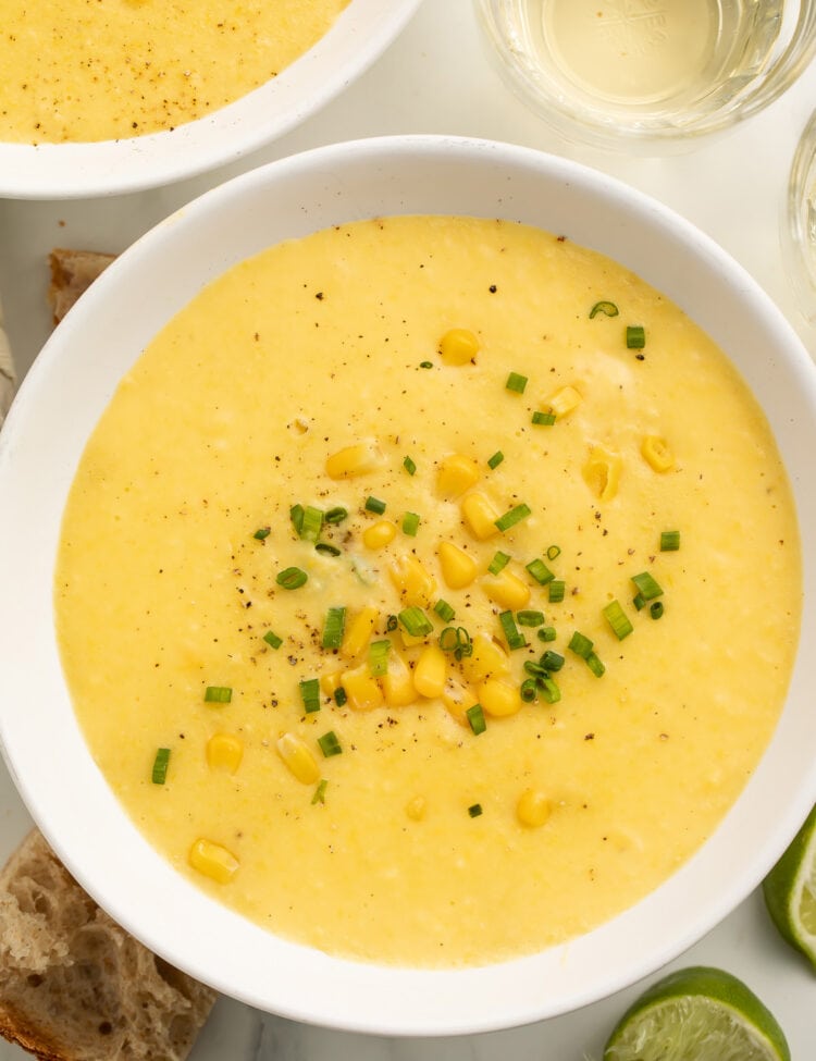 A white soup bowl holding a thick, creamy yellow corn soup topped with corn kernels and chopped green onions.
