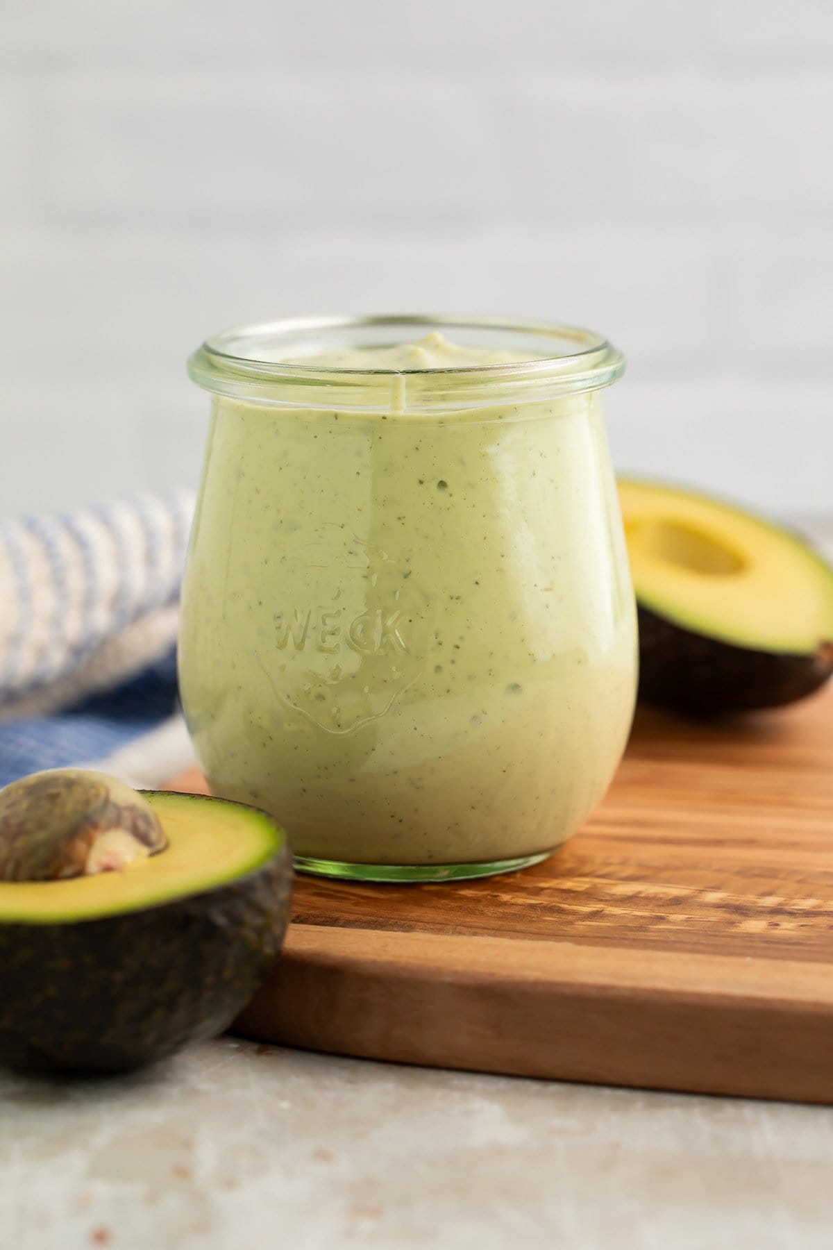 Creamy avocado ranch dressing in a jar sitting on a wooden cutting board next to two avocado halves.