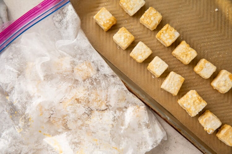 Coated tofu cubes in a zippered plastic bag next to a baking sheet lined with tofu cubes